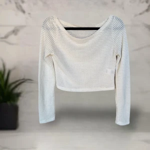Vit croppad topp  - Säljer en vit croppad topp  i storlek S. Toppen har lång ärm och är tillverkad i ett luftigt, stickat polyestermaterial med struktur. Perfekt för dig som gillar en enkel men trendig look med lite extra edge tack vare den croppade passformen.