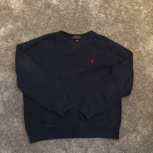 Mörkblå sweatshirt från Polo Ralph Lauren - Klassisk mörkblå sweatshirt från Polo Ralph Lauren med röd broderad logga på bröstet. Tröjan har rund halsringning, långa ärmar och ribbade muddar. Perfekt för en stilren och avslappnad look. Inga tecken på fläckar eller defekter, skick 8/10.  Nypris ca 1000kr säljs för 300kr. Pris kan diskuteras.passar dig mellan 160-165