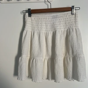 Vit volangkjol från Gina Tricot - Supersöt vit kortkjol från Gina Tricot i storlek XS. Kjolen har smockad midja och flera volanger som ger en flowy och luftig känsla. Perfekt för dig som gillar en feminin och trendig stil. Materialet är lätt och känns skönt mot huden. Om du köper denna tillsammans med annonsen efter denna kan du få båda för 80!