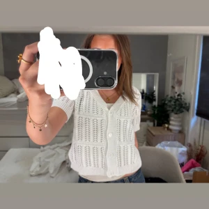 Vit stickad kortärmad kofta med knappar - Säljer en söt vit stickad blus med korta ärmar och v-ringning. Blusen har ett luftigt hålmönster och stora vita knappar framtill. Perfekt att styla med jeans eller kjol för en fräsch look.