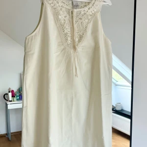 Slt klänning med spets från Vila - Superfin vit kortklänning från Vila med spetsdetaljer och knytning vid halsen. Klänningen är ärmlös och har en lös passform, perfekt för varma dagar. Storlek M. Hängt i garderoben.