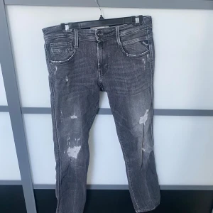 Replay anbass  - Snygga grå jeans från Replay med slitna detaljer och lagningar på benen. Klassisk femficksmodell med raka ben och tydliga sömmar. Jeansen har en cool, tvättad look och Replay-logga på fickan. 