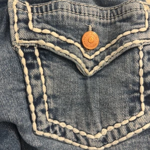 Blå jeans med kontrastsömmar - Snygga blå jeans med vita, grova kontrastsömmar och coola ficklock bak med kopparfärgade knappar. Jeansen har klassisk passform och raka ben, tillverkade i slitstarkt denim. Perfekta för dig som vill sticka ut med detaljer.