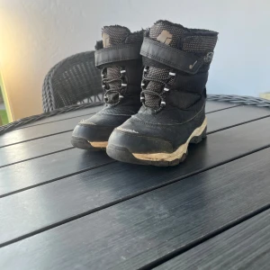 Svarta vinterstövlar med snörning, strl 30 - Svarta vinterstövlar med grov sula och snörning framtill. Insidan är fodrad med mjukt material för extra värme. Stövlarna har kardborreband upptill och är perfekta för kalla dagar. Snygg och praktisk design med slitstark syntet och textil.