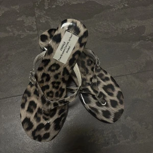 Leopardmönstrade sandaler med hjärtdetalj - Snygga sandaler med leopardmönster och glittrande hjärtdetalj på remmen. Skorna har en liten platåsula och remmar i silverfärgad syntet. Perfekta för att sticka ut i sommar med sin djurmönstrade look.