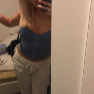 Blå korsett-topp - Säljer en blå korsett-topp med snygg, vågig kant upptill och croppad passform. Toppen är ärmlös och har en figurnära siluett som framhäver midjan. Perfekt att styla med jeans eller kjol för en trendig look.
