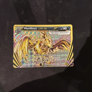 Mandibuzz BREAK - En glittrande och exklusiv Mandibuzz BREAK Pokémonkort med 140 HP. Kortet har en cool guld-design och attacken 'Wings of Disaster'. Perfekt för samlare och Pokémon-fans som vill stärka sin kortlek med något unikt!