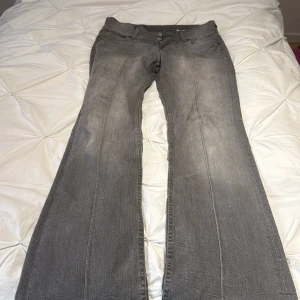 Grå bootcut jeans från Bershka - Säljer ett par gråa jeans från Bershka i storlek 38. Modellen har bootcut-ben och klassisk femficksdesign med knapp och dragkedja framtill. Jeansen har en snygg tvättad look och är tillverkade i mjukt denim-material.