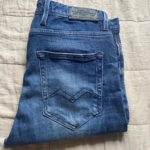 Replay Anbass jeans blå - Säljer ett par Replay Anbass jeans i snyggt blått med slitningar och skinny fit. Klassisk femficksmodell med coola detaljer på bakfickorna och logga på linningen.       Storlek 29/32