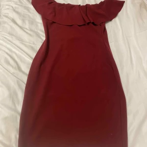 Vinröd offshoulder klänning stl 10 - NYYYYY OANVÄND!Snygg vinröd klänning i offshoulder-modell med bred volang upptill. Klänningen är figurnära och tillverkad istretchigt material av polyester och elastan. Perfekt för dig som vill sticka ut med en elegant och trendig look.