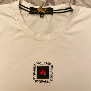 Dsquared2 t-shirt  - Stilren vit t-shirt från Dsquared med klassiskt tryck på bröstet med röd lönnlöv och D2-logga. I nytt skick, inga defekter och behöver bara strykas. Storlek M, självklart äkta. Säljer billigt! 