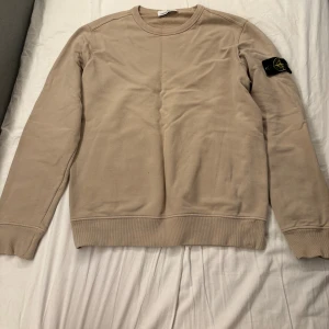 Beige Stone Island sweatshirt - Säljer en beige sweatshirt från Stone Island med klassisk rund krage. Tröjan har Stone Island-loggan på vänster ärm. Perfekt basic med snygg passform och stilren look.
