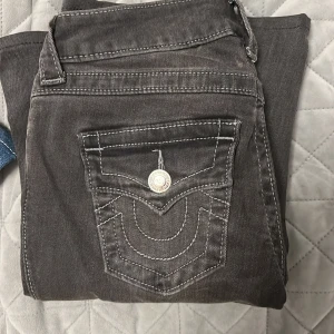 True Religion Joey Low Rise Flare Jeans - Säljer ett par mörkgrå True Religion Joey Low Rise Flare jeans med vita kontrastsömmar och snygga detaljer på bakfickorna. Modellen har låg midja och utsvängda ben. köpta för 1200kr o är nästan o andvända. pris kan diskuteras 
