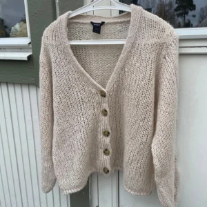 Beige stickad kofta från Lindex - Mysig beige stickad kofta från Lindex i storlek S. Koftan har grovstickat material, snygga flätade detaljer på ärmarna och fem stora knappar framtill. V-ringad hals och långärmad modell som ger en chill och avslappnad vibe.