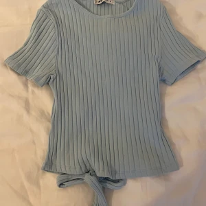 Gullig topp - Jättesöt topp med knytning i ryggen från New Yorker i en fin blå färg. Den är i skönt ribbat material men har två små fläckar framtill, men skulle inte säga att de syns speciellt mycket!