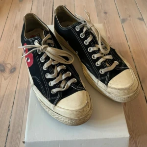 Converse x Comme des Garçons Play sneakers - Svarta Converse Chuck Taylor sneakers i samarbete med Comme des Garçons Play. Skorna har en ikonisk röd hjärtlogga på sidan, vita kontrastsömmar och beige snörning. Platt sula och rund tå, tillverkade i bomullstextil. Perfekt för dig som gillar streetstyle och coola detaljer.
