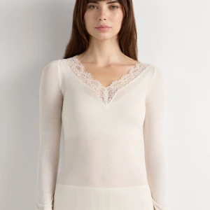 Vit långärmad topp med spetsdetaljer - Superfin vit långärmad topp med v-ringning och spetsdetaljer längs halsringningen och ärmsluten. Tunn och mjuk i materialet, perfekt för lager-på-lager. Snygg och feminin look med genomskinlig känsla och smickrande passform.