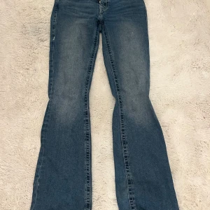Blå Becca bootcut jeans med strass - Snygga blå bootcut jeans från true religon  i modell becca o dom är lowwaist. Baksidan har coola fickor med  glittriga knappar. Perfekt för dig som gillar lite extra bling på dina jeans. har bara använts 1 gång och dom är nästan helt nya och är i jätte bra skick. dom köptes för 1800