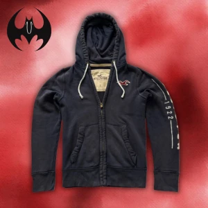 Blå hoodie med dragkedja från Hollister  - Blå hoodie med dragkedja och en stor vit markerade text  ’Hollister’ | size S | längd: 66cm Arm: 68cm Axelbredd: 46cm | Passar mellan 170-185 cm