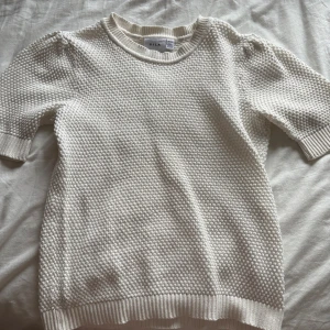 Vit stickad kortärmad tröja från Vila - Säljer en vit stickad tröja från Vila i storlek XS. Tröjan har korta ärmar, rund halsringning och ett snyggt strukturmönster över hela plagget. Perfekt för lager-på-lager och passar till både jeans och kjol.