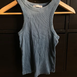 Blå ribbad linnetopp från Zara - Säljer en blå ribbad linnetopp från Zara med rund hals och ärmlös design. Toppen har en slim passform och är tillverkad i mjuk bomull som känns skön mot huden. Perfekt för dig som gillar enkel och stilren look.