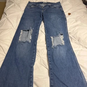 Blå bootcut jeans från 157 med slitningar - Säljer ett par blå bootcut jeans från 157 med stora slitningar på båda knäna. Jeansen har klassisk femficksdesign, normal midja och är tillverkade i denim. Perfekta för dig som gillar en avslappnad och trendig look.