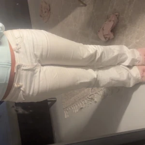 Vita bootcut jeans med låg midja - Säljer ett par vita jeans med klassisk femficksdesign och låg midja. Modellen har bootcut-ben som ger en snygg siluett och är tillverkade i ett mjukt bomullsmaterial. 