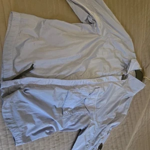 Ljusblå overshirt från C.P. Company - Snygg ljusblå overshirt från C.P. Company med klassisk krage och långa ärmar. Tillverkad i multifilament återvunnen nylon med meshfoder, vilket ger en lätt och modern känsla. Fickor framtill och diskreta knappar. Perfekt för dig som gillar stilrena och funktionella plagg och den är helt oanvänd.