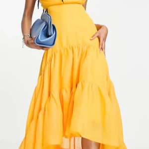 Gul volangklänning med asymmetrisk fåll - Superfin gul klänning med volanger och asymmetrisk fåll. Klänningen har en luftig och flowy känsla, perfekt för varma dagar. Den är ärmlös och har en snygg passform som framhäver midjan. Materialet känns lätt och bekvämt.