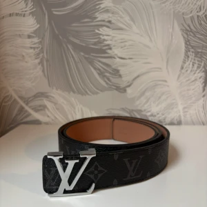 Svart bälte med silver logga - Fin helt ny svart bälte med silver logga. 115cm lång. Med bältet så får man med ett liter metall verktyg man kan göra hål med hjälp av hammare. Tveka inte att dm:a vid frågor eller intresse!