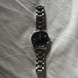 Svart och silver klocka från Justcavalli - Stilren klocka från justcavalli med svart urtavla och silverfärgat armband i metall. Klockan har romerska siffror vid tolv och sex, samt tydliga indexmarkeringar. Länkat armband och klassisk rund form ger en tidlös look.