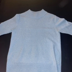 Ljusblå polotröja från VILA - Superskön ljusblå polotröja från VILA i storlek S. Tröjan har en hög krage, långa ärmar och breda ribbade muddar vid hals, ärmslut och nederkant. Materialet är mjukt och stickat, perfekt för kyliga dagar. Enkel och stilren design som är lätt att matcha.