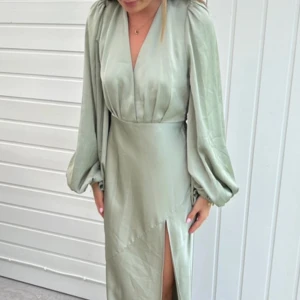 Balklänning  - Super fin ljusgrön långklänning i satin med v-ringning, ballongärmar och slits framtill. Klänningen har öppen rygg med knytband i nacken och en elegant, figurnära passform. Köpt av Hilma stille och säljer då den tyvärr inte passade mig. Nypris är ca 3000kr