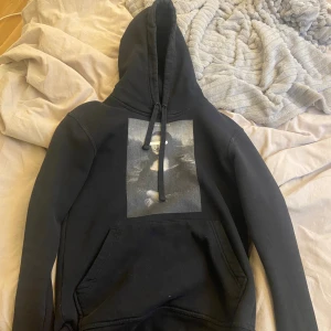 Mona Lisa hoodie  - Svart hoodie från The Cool Elephant i storlek XS. Tröjan har en stor huva med snörning och en tryckt bild på framsidan. Klassisk känguruficka framtill och mjukt material som känns skönt mot huden. Perfekt för chill dagar och streetstyle.