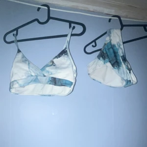 Blåvit bikini med marmor-mönster - Säljer en snygg bikini i blått och vitt med marmor-liknande mönster. Överdelen har justerbara axelband och omlott-skärning framtill. Underdelen är klassisk med samma mönster. Materialet känns som syntet och är ribbat för extra stil.