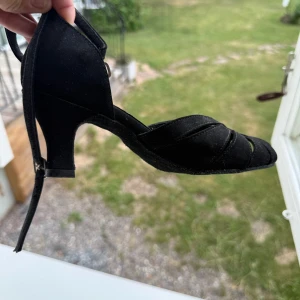 Svarta klackskor - Svarta klackskor för dans eller användning i vardagen köpta i dansbutiken. Lite osäker på storlek men passar mig som har 36. Snygg design med remmar över foten och öppen tå. Skorna har en smal rem runt vristen med spänne och är tillverkade i mockaliknande material. Perfekta för dig som vill ha en elegant och stilren look.