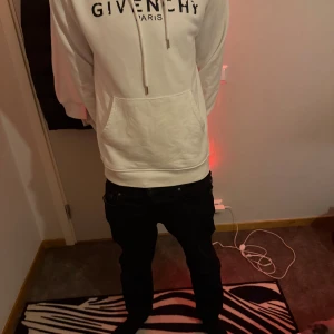 Vit Givenchy hoodie med tryck - Säljer en clean vit hoodie från Givenchy med svart logotyp-tryck på bröstet. Hoodien har huva med snörning och en stor magficka framtill. Mjuk och skön passform, perfekt för dig som gillar stilrena streetwear-plagg.