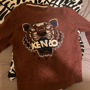 Brun Kenzo sweatshirt med tigertryck - Säljer en brun sweatshirt från Kenzo med ikoniskt broderat tigerhuvud och logga på bröstet. Tröjan har rund halsringning och långa ärmar. Perfekt statement piece för dig som vill sticka ut med cool design.