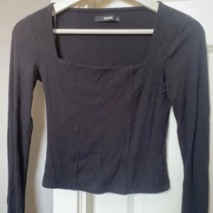 Svart långärmad topp från Bik Bok - Svart långärmad topp från Bik Bok med fyrkantig halsringning och ribbad struktur. Snygg och enkel design som är lätt att matcha med olika outfits. Materialet är mjukt och stretchigt för en bekväm passform.