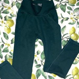 Mörkgröna leggings från Tridri - Mörkgröna leggings från Tridri med hög midja och tight passform. Perfekta för träning eller chill, tillverkade i ett stretchigt syntetmaterial som sitter skönt mot kroppen. Stilrena utan synliga detaljer eller mönster.