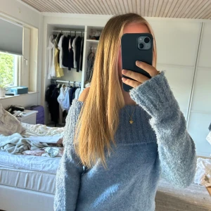 Ljusblå offshoulder stickad tröja - Supermysig ljusblå stickad tröja med offshoulder-design och bred ribbad kant upptill. Tröjan har långa ärmar och är fluffig i materialet, perfekt för kyliga dagar. Snygg att styla med jeans eller kjol för en chill look.