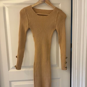 Beige ribbad långklänning med knappar - Snygg beige ribbad långklänning med lång ärm och coola guldknappar längs ärmslut och nedtill på klänningen. Klänningen har en tight passform och en liten slits nertill. Använd endast en gång! Skriv för fler bilder🥰
