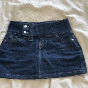  Ny Mörkblå jeanskjol från Bershka - Snygg mörkblå jeanskjol från Bershka med , två knappar framtill och klassiska fickor. Kjolen har en rak passform och tydliga kontrastsömmar som ger en cool denimlook. Perfekt för dig som gillar en enkel men trendig stil.
