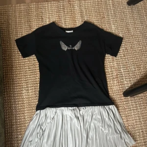 Svart och silver klänning LC Waikiki - Cool klänning från LC Waikiki med svart överdel och tryckta vingar samt texten 'Be Special' framtill. Kjoldelen är plisserad i skimrande silverfärg. Kortärmad och med rund hals, perfekt för dig som gillar kontraster och detaljer.