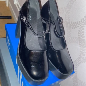 Svarta Mary Jane-klackar från ASOS - Säljer ett par svarta Mary Jane-klackar från ASOS med bred klack och platåsula. Skorna har rund tå, spänne över foten och är tillverkade i glansigt syntetmaterial. Perfekta för dig som vill ha en edgy och trendig look. Endast använd 2 gånger. Köpta för 380. Pris kan diskuteras!