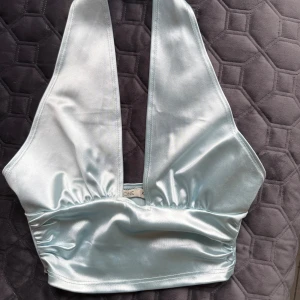 Ljusblå satin top  - Ljusblå top i satin. Dragkedja på sidan och knappar i nacken. Går att använda korsad eller inte. Oanvänd med ingen lapp kvar