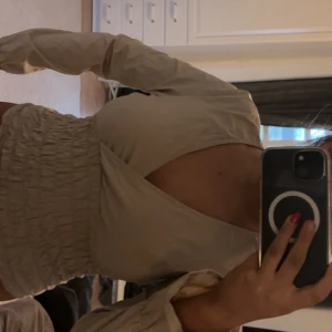 Beige omlottblus från ONLY - Säljer en beige omlottblus från ONLY i storlek M. Blusen har lång ärm, v-ringning och smockad midja som ger en snygg passform. Materialet är lätt och känns skönt mot huden. Perfekt för dig som gillar stilrena och trendiga plagg.