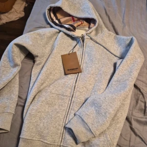 Grå bruberry hoodie - Snygg grå hoodie från Burberry i storlek S med klassiskt rutigt foder i huvan och broderad logga på bröstet. Tröjan är helt oanvänd. Säljer för att den är för liten. Pris kan diskuteras.
