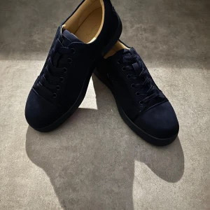 Mörkblåa Christian Louboutin sneakers mocka - Snygga mörkblå sneakers från Christian Louboutin i mjuk mocka med klassisk röd sula och broderad logga bak. Skorna har rund tå, snörning och en stilren design som sticker ut med exklusiva detaljer och lyxig känsla.