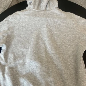 Grå hoodie från H&M, relaxed fit - En stilren ljusgrå hoodie från H&M i relaxed fit. Tröjan har huva, magficka och långa ärmar. Perfekt för chill dagar eller när du vill ha en enkel och clean look. Materialet är mjukt och skönt, troligtvis bomullsmix.